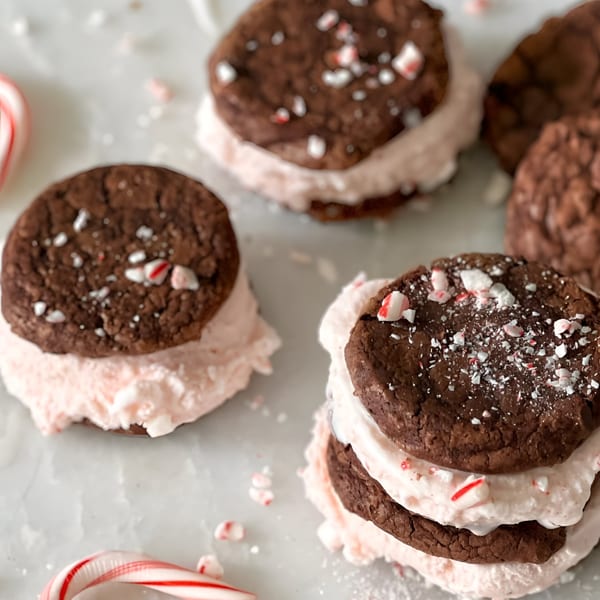 Chocolate cookies with pink frosting and crushed candy canes, with whole candy canes nearby.