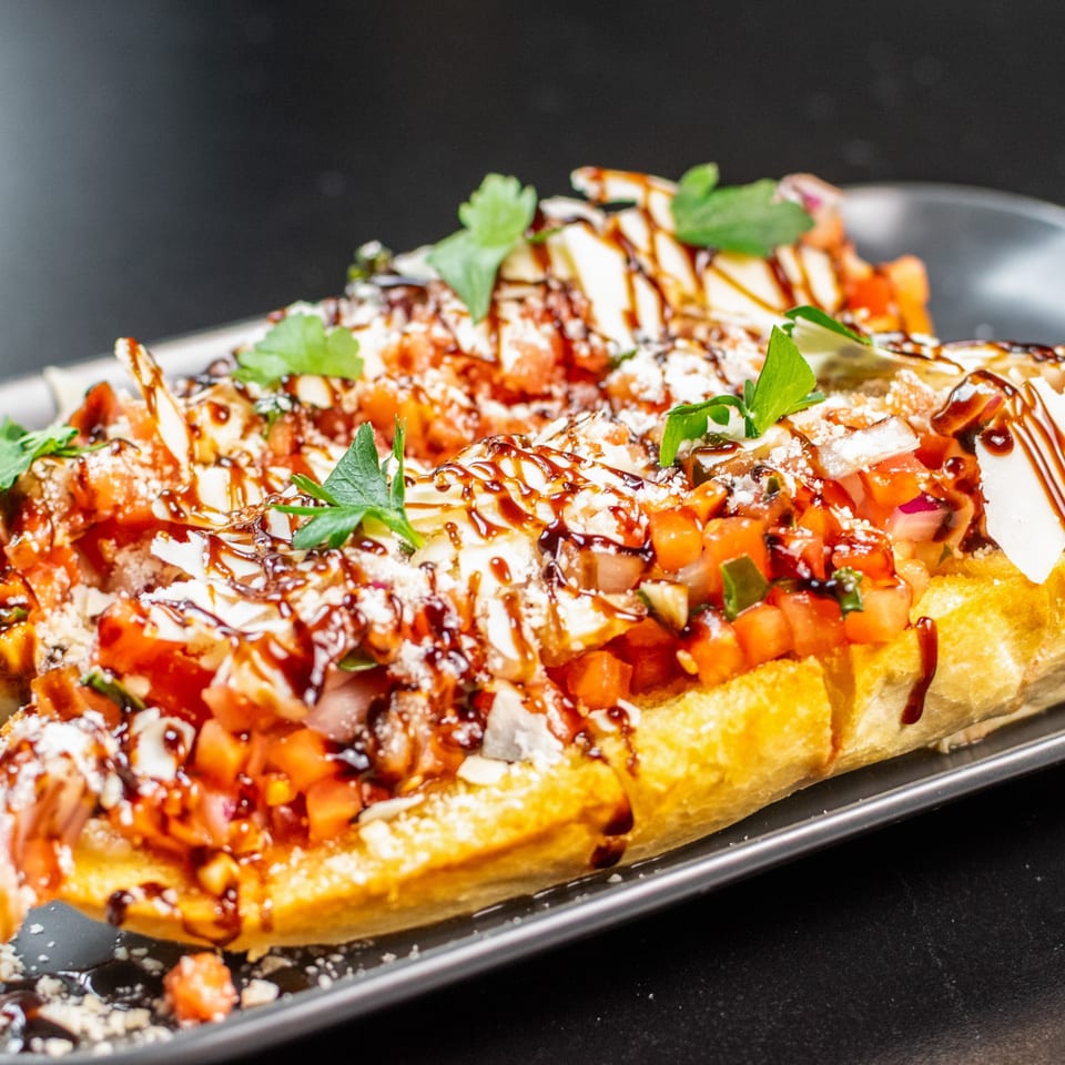 Close-up of two bruschetta halves topped with diced tomatoes, cheese, herbs, and balsamic glaze.