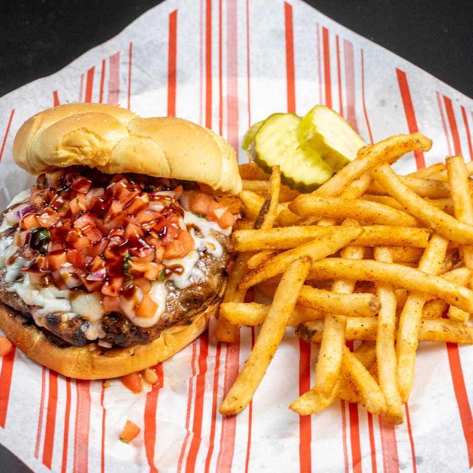 A Wise Guys Downtown burger with melted cheese, diced tomatoes, and balsamic glaze, served with fries and pickles.