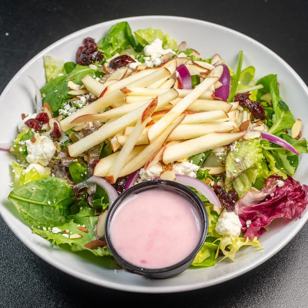 Fresh Italian salad with mixed greens, apple slices, goat cheese, cranberries, and a side of pink dressing.