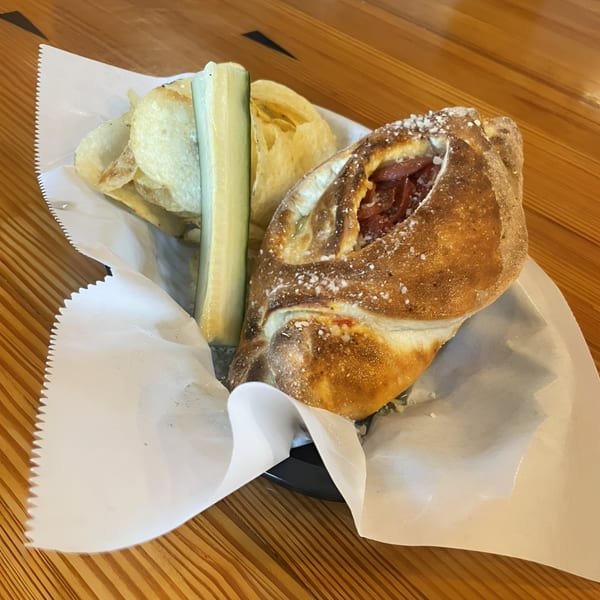 Calzone with chips and a pickle spear in a paper-lined basket on a wooden table.