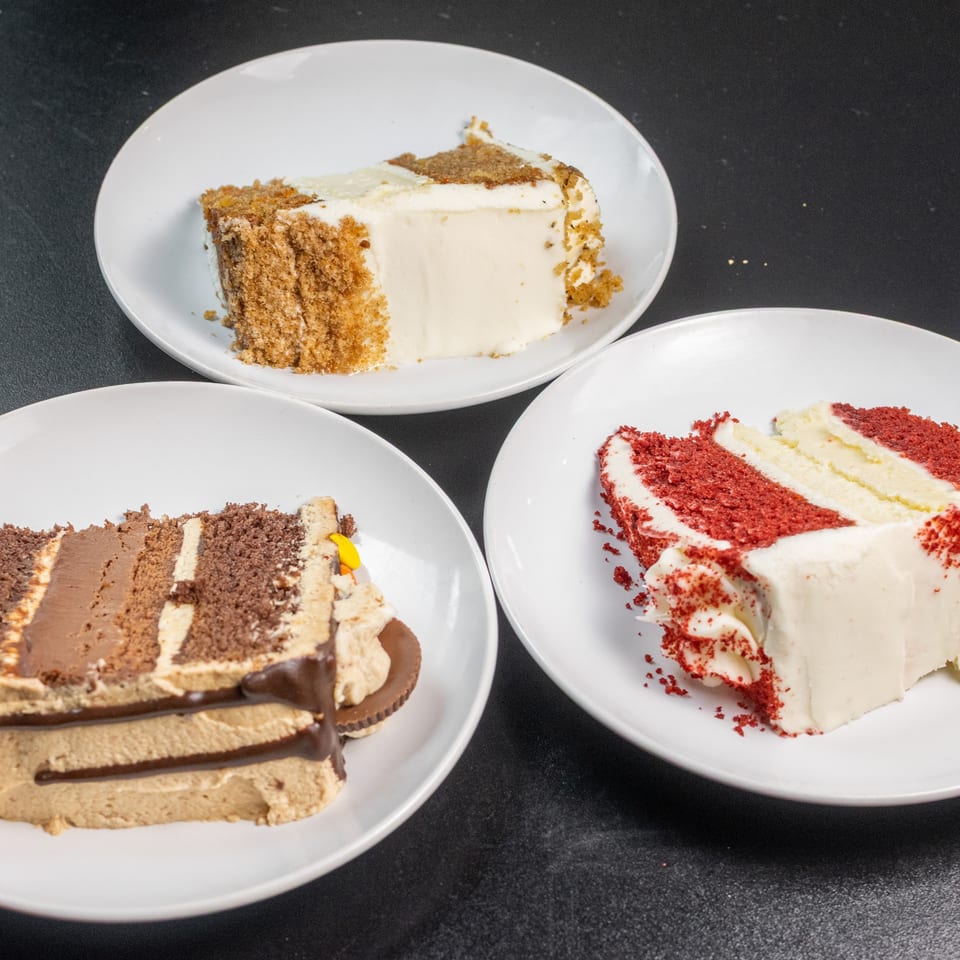 Three slices of cake on white plates: carrot cake, chocolate peanut butter cake, and red velvet cake.